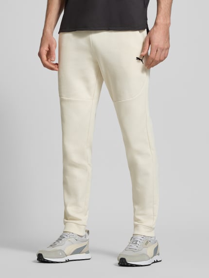 Männermodel trägt Regular Fit Sweathose mit Logo-Print Modell 'Pumatech' von PUMA PERFORMANCE aus Baumwoll-Mix, Eingrifftaschen, elastischer Bund, helle Farbe, Ganzkörperansicht von vorne.