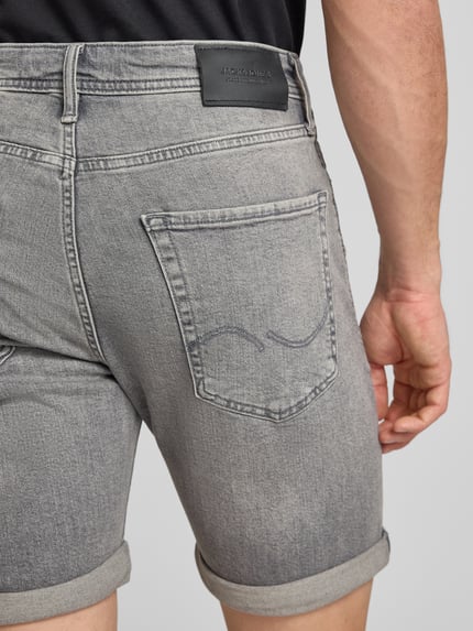 Männermodel trägt Regular Fit Jeansshorts mit Umschlag Modell 'RICK' von Jack & Jones aus grauem Baumwoll-Elasthan-Mix, Nahaufnahme Rückansicht. Herren Jeansshorts mit Eingrifftaschen, Bundweite bei Größe M 42 cm, Innenbeinlänge 21 cm.