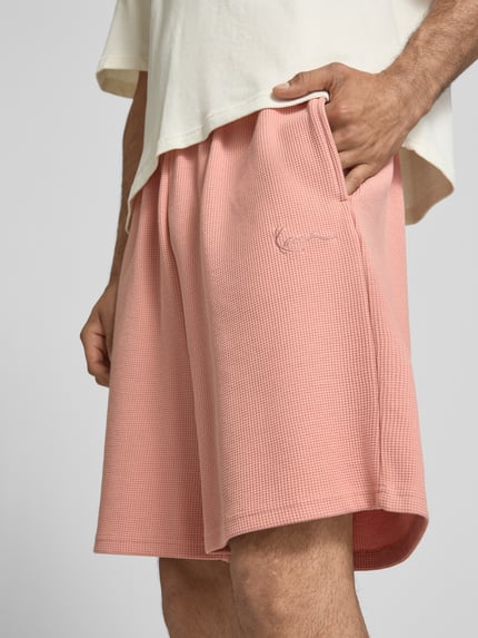 Männermodel trägt Regular Fit Shorts mit Strukturmuster von KARL KANI in Rosa, Baumwoll-Mix, Logo-Stitching, Nahaufnahme Oberschenkel.