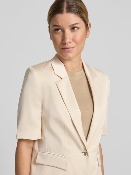 Vrouwenmodel draagt Slim Fit Blazer mit 1/2-Arm van SWING in licht beige met reverskraag en klepzakken, detailopname bovenlichaam, lengte achterzijde maat 36: 58 cm.