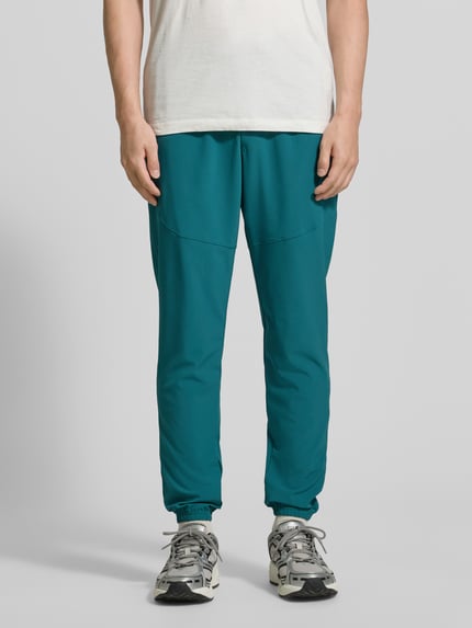 Männermodel trägt Regular Fit Jogger mit Logo-Print Modell 'Vibe' von Under Armour in Türkis, elastischer Bund, Eingrifftaschen, Ganzkörperansicht von vorne.