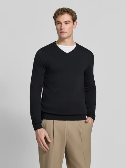 Männermodel trägt Pullover mit Logo-Stitching von S.OLIVER CASUAL in Schwarz, Strickstruktur, V-Ausschnitt, ganzkörperansicht von vorne.