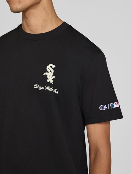 Männermodel trägt Relaxed Fit T-Shirt aus reiner Baumwolle von Champion in Schwarz mit weißem Statement-Print, Label-Stitching, Nahaufnahme Oberkörper. Rückenlänge bei Größe M: 70 cm.