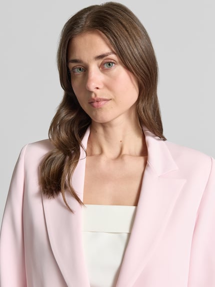 Frauenmodel trägt Blazer mit Reverskragen Modell 'REWI' von Rinascimento in hellrosa, Material-Mix, Nahaufnahme Oberkörper.