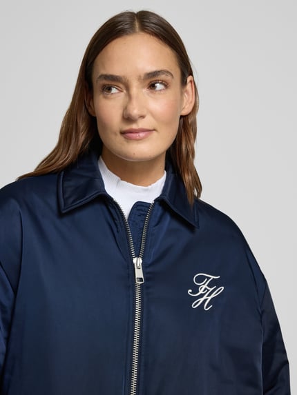 Modelka kobieca nosi granatową Regular Fit Bomberjacke mit Logo-Detail od Tommy Hilfiger, jednolity kolor, zbliżenie na górną część ciała.