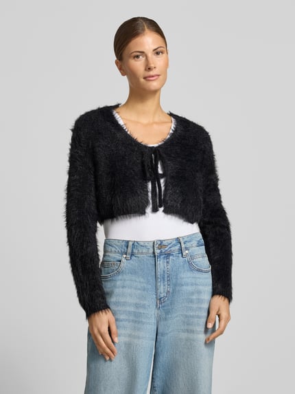 Modelka nosi Regular Fit Bolero mit Zierschleife od Apricot, czarny, wygląd dzianiny, krój regular fit, kokarda, cropped fit, długość tyłu w rozmiarze S: 39 cm, długość rękawa w rozmiarze S: 64 cm, widok całej sylwetki z przodu