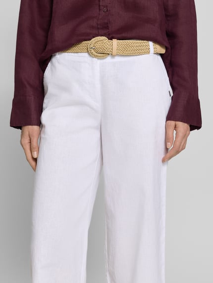 Frauenmodel trägt Culotte aus Leinen-Mix mit Gürtel von Christian Berg Woman in Weiß, weiter Schnitt, französische Taschen, Nahaufnahme Oberkörper.