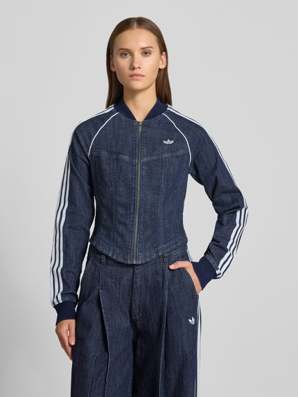 Kobieta model prezentuje kurtkę jeansową Regular Fit Jeansjacke aus Baumwoll-Mix model 'SUPERSTAR' od adidas Originals, widok na górną część ciała z przodu.