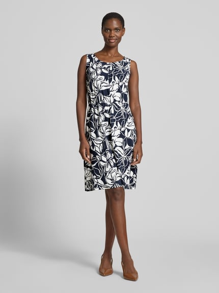 Modelka nosi Knielanges Kleid aus Viskose-Mix mit Rundhalsausschnitt von Betty Barclay, mieszanka wiskozy z dodatkiem streczu, taliowany fason, długość do kolan, okrągły dekolt, wycięcie w kształcie łezki z wiązaniem z tyłu, długość tyłu w rozmiarze 36: 97 cm, szerokość w rozmiarze 36: 39 cm, ciemne i jasne wzory kwiatowe, gładka faktura, widok całej sylwetki z przodu.