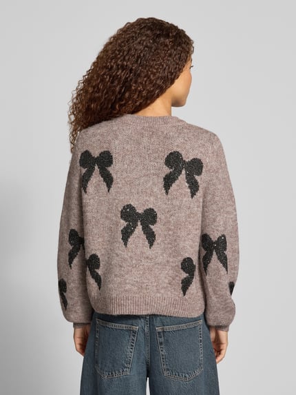 Frauenmodel trägt Pullover mit Glitzer Schleifen-Details von ONLY in Melange Strickoptik, glänzender Motiv-Print, Ganzkörperansicht Rückansicht.