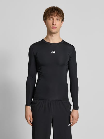 Męski model nosi Longsleeve mit Label-Print od adidas Training, materiał z domieszką stretchu, krój slim fit, czarny kolor, widok całej sylwetki z przodu.