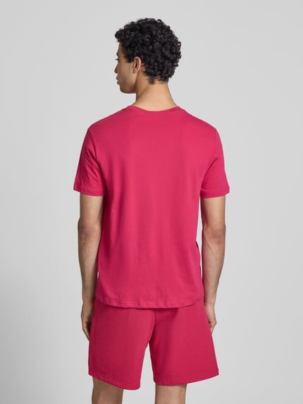 Männermodel trägt T-Shirt mit Label-Print und Rundhalsausschnitt von CHAMPION in Pink, reine Baumwolle, Regular Fit, Ganzkörperansicht Rückansicht.