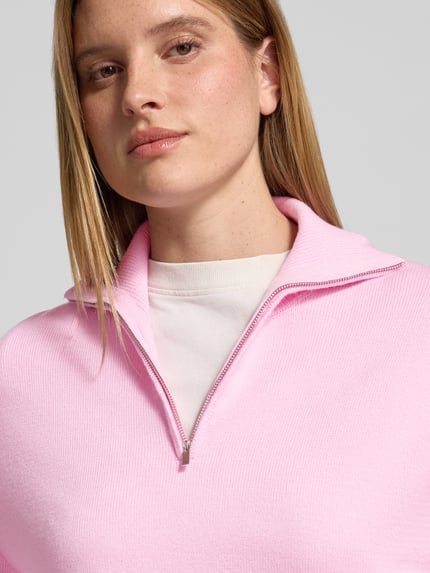Frauenmodel trägt Troyer mit halblangem Reißverschluss Modell 'RIZIN' von MANGO in Rosa, Feinstrick mit Strukturmuster, Nahaufnahme Oberkörper.