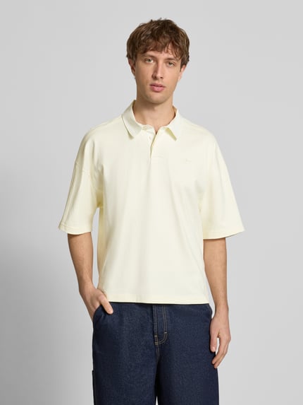 Männermodel trägt Regular Fit T-Shirt mit Polo-Kragen von adidas Originals in Creme, reine Baumwolle, Logo-Stitching, Ganzkörperansicht von vorne.