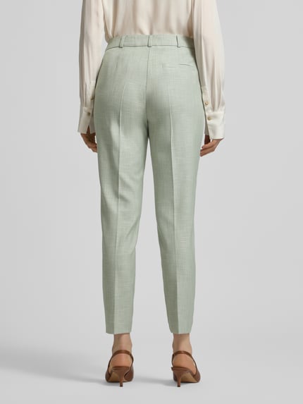 Frauenmodel trägt Slim Fit Stoffhose aus Viskose-Mix mit Bügelfalten von Comma, helle grüne Farbe, Gesäßtasche, Haken-Reißverschluss, Ganzkörperansicht Rückansicht.