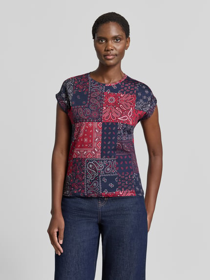 Vrouwenmodel draagt t-shirt met ronde hals van Christian Berg Woman, puur katoen, getailleerde pasvorm, rode en blauwe patchworkprint, vaste mouwomslagen, ruglengte maat S 55 cm, geheel vooraanzicht.