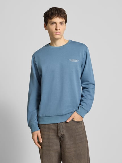 Männermodel trägt Sweatshirt mit Label-Print von Jack & Jones in Blau, lockerer Schnitt, Rundhalsausschnitt, Nahaufnahme Oberkörper.