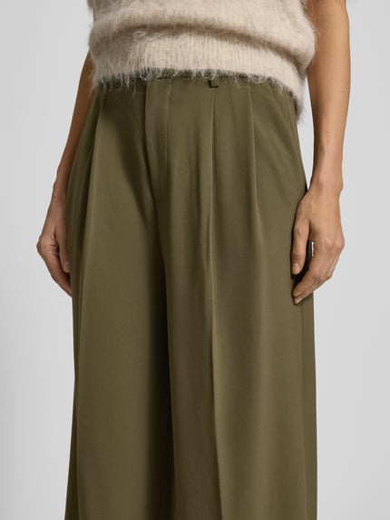 Frauenmodel trägt Stoffhose mit Bundfalten Modell 'Charlize' von MOS MOSH in Olivgrün, lockerer Schnitt, Nahaufnahme Oberkörper. Material-Mix mit Stretch, französische Eingrifftaschen und Gesäßtasche sind sichtbar.