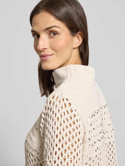 Vrouwenmodel draagt Strickpullover aus Viskose-Mix met pailletten van monari in crème, regular fit, col, details op mouwen, half close-up zijaanzicht.
