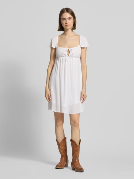 Frauenmodel trägt Babydoll Kleid aus Viskose mit Karree-Ausschnitt und Schleife von REVIEW, Gerader-Schnitt, Minikleid, Ganzkörperansicht von vorne.