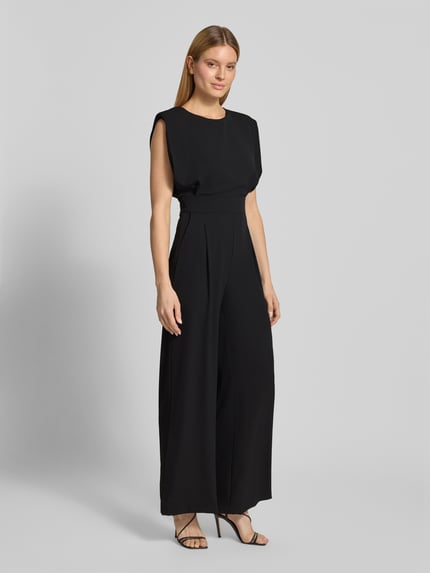 Modelka kobieca nosi Regular Fit Jumpsuit mit Rundhalsausschnitt od Rinascimento, czarny, bez rękawów, z zakładkami, krój regular fit z elastycznego materiału, długość całkowita 150 cm, szerokość w rozmiarze S: 45 cm, długość pleców: 50 cm, długość nogawki wewnętrznej: 86 cm, widok całej sylwetki z przodu.