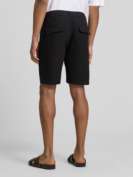 Männermodel trägt Bermudas aus Leinen-Mix mit französischen Eingrifftaschen von Lindbergh, schwarze Farbe, Ganzkörperansicht Rückansicht, Leinen-Baumwoll-Mix, Straight Fit, elastischer Bund mit Kordelzug, Knopf- und Reißverschluss, Gesäßtaschen, Bundweite bei Größe M 43 cm, Innenbeinlänge bei Größe M 24 cm.