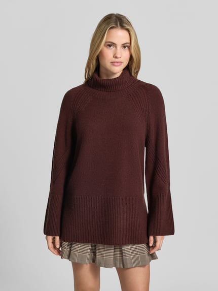 Frauenmodel trägt Oversized Pullover aus reinem Kaschmir von Joseph in Dunkelrot, Strick-Optik, Rollkragen, gerippte Abschlüsse, Ganzkörperansicht von vorne.