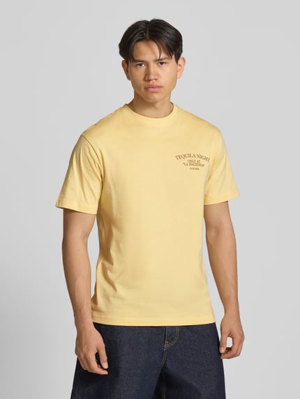 Männermodel trägt Regular Fit T-Shirt aus reiner Baumwolle Modell 'FRED' von Only & Sons in Optik: Unifarben mit Motiv-Print, Rundhals-Ausschnitt, Ärmelform: Kurzarm, Materialverarbeitung: Jersey, Ganzkörperansicht von vorne.