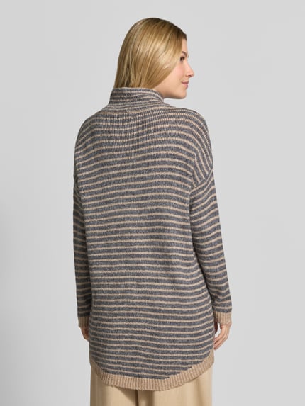 Frauenmodel trägt Oversized Fit Strickpullover mit Viskose-Anteil von Apricot in Beige und Grau, verlängerte Rückseite, Ganzkörperansicht Rückansicht.
