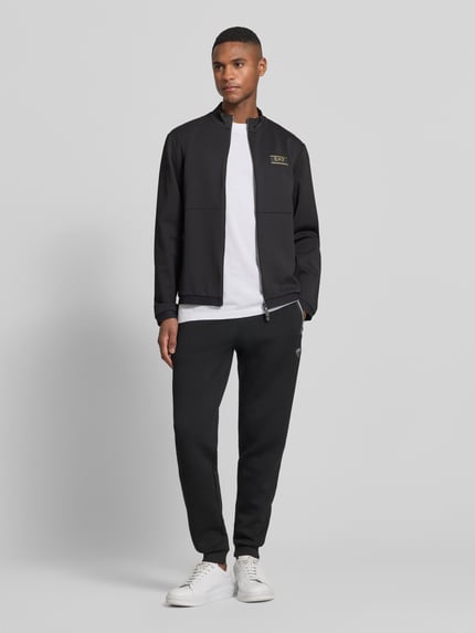 Männermodel trägt schwarze Sweatjacke mit Zweiwege-Reißverschluss von EA7 Emporio Armani, Material-Mix mit Viskose-Anteil, Regular-Fit, Stehkragen, Reißverschlusstaschen, Label-Patch; Ganzkörperansicht von vorne.