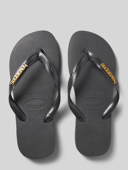 Produktfoto, Zehentrenner mit Label-Detail von Havaianas in Schwarz mit goldfarbenem Logo, flache Sohle, Damenmodell, strukturierte Oberfläche