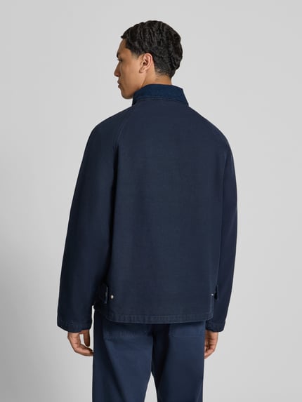 Męski model nosi Regular Fit Jacke mit Umlegekragen od Forét z bawełny, wpuszczane kieszenie, zapięcie na klamrę, krój regular fit, długość tyłu 70 cm, szerokość ramion 45 cm, długość rękawów 70 cm, kolor granatowy, tekstura gładka, pełny widok z tyłu.