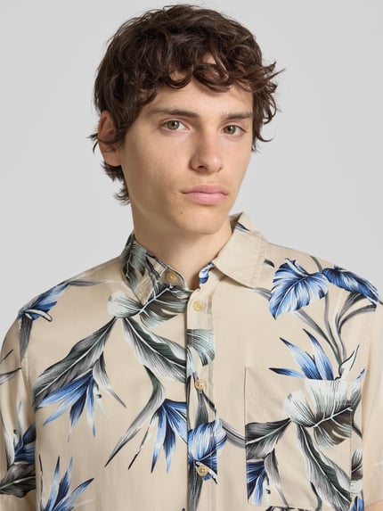 Männermodel trägt Regular Fit Freizeithemd aus Viskose Modell 'AMELO' von Blend mit Allover-Blumenmuster in Beige, Blau und Schwarz, Nahaufnahme Oberkörper.