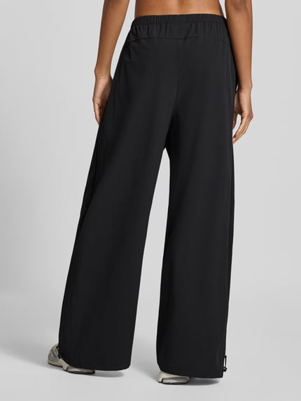 Frauenmodel trägt Regular Fit Trainingshose mit Bundfalten von adidas Sportswear in schwarz mit Struktur, Wide Leg, High Waist, Logo-Print, Ganzkörperansicht Rückansicht