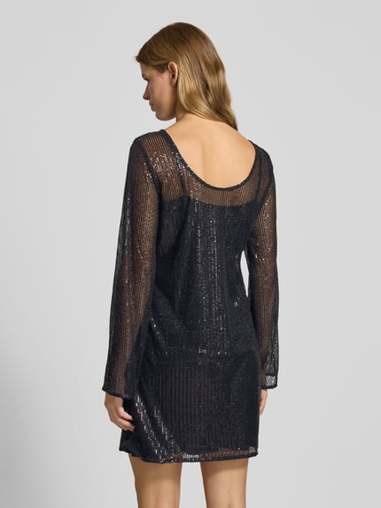 Frauenmodel trägt fließendes Cocktailkleid mit Paillettenbesatz Modell 'JACK' von Pieces in schimmernder, semitransparenter Optik, Mini-Länge, U-Boot-Ausschnitt, Langarm, gerader Saum, Ganzkörperansicht Rückansicht.
