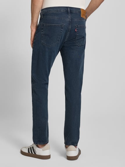 Männermodel trägt Tapered-Fit Jeans aus Baumwoll-Mix Modell '502™ TAPER' von Levi's® in dunklem Blau mit Taschenstruktur, Ganzkörperansicht Rückansicht. Herren Tapered Fit Jeans von Levi's®.