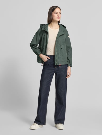 Vrouwenmodel draagt Jacke mit Zweiwege-Reißverschluss Modell 'DOLORES NEO' van Frieda & Freddies in katoenmix, recht model, capuchon met koordstoppers, tweewegritssluiting, labelpatch, klepzakken met knoopsluiting, elastische mouwboorden, verstelbare zoom met koordstoppers, ruglengte maat 36: 59 cm, schouderbreedte: 48 cm, borstwijdte: 50 cm, mouwlengte: 52 cm, kleur groen, hele lichaamsaanzicht van voren.