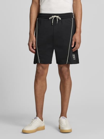 Männermodel trägt Regular Fit Sweatshorts aus Baumwoll-Mix Modell 'DARYNTO' von HUGO in Optik: Unifarben mit Kontraststreifen, Logo-Stitching, elastischem Bundabschluss mit Tunnelzug und seitlichen Eingrifftaschen vorne, Materialverarbeitung: Sweat, Vorderansicht, Nahaufnahme Unterkörper.