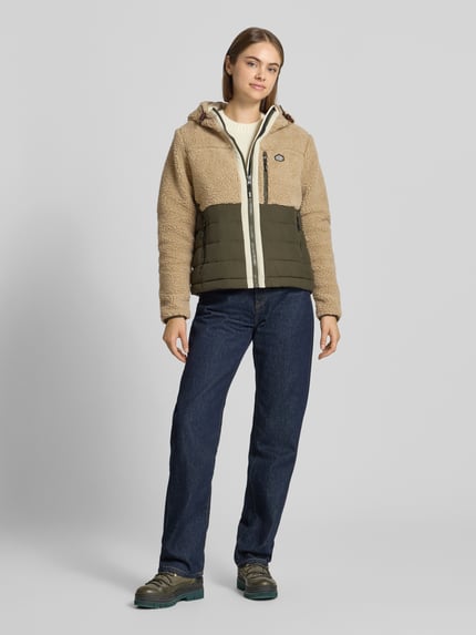 Kobieta modelka nosi Regular Fit Jacke mit Teddyfellbesatz od Superdry, beżowy i oliwkowy kolor, kaptur z tunelem, zamek błyskawiczny, kieszenie napoleonki i wpuszczane, długość tyłu w rozmiarze S: 58 cm, szerokość ramion w rozmiarze S: 42 cm, szerokość w rozmiarze S: 44 cm, długość rękawów w rozmiarze S: 63 cm, widok całej sylwetki z przodu.