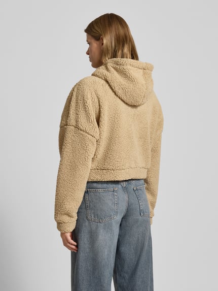 Kobiece model prezentuje Kurtka z futerka o krótkim kroju Model 'CUDDLE' od Noisy May, luźny krój, kaptur, tunel, zamek błyskawiczny, wpuszczane kieszenie, długość tyłu 48 cm, szerokość ramion 79 cm, szerokość klatki piersiowej 77 cm, długość rękawów 48 cm, jasny beż, tekstura pluszu, widok całej sylwetki z tyłu.