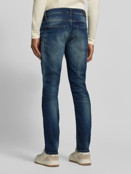 Männermodel trägt Slim Fit Jeans mit Label-Patch Modell 'DELAWARE BO' von BOSS Orange in Medium Wash Denim, Ganzkörperansicht Rückansicht.