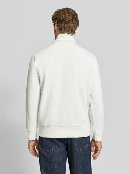Männermodel trägt weißen Regular Fit Troyer aus Baumwoll-Mix von GANT, glatte Textur, dunkle Jeans, Ganzkörperansicht Rückansicht.