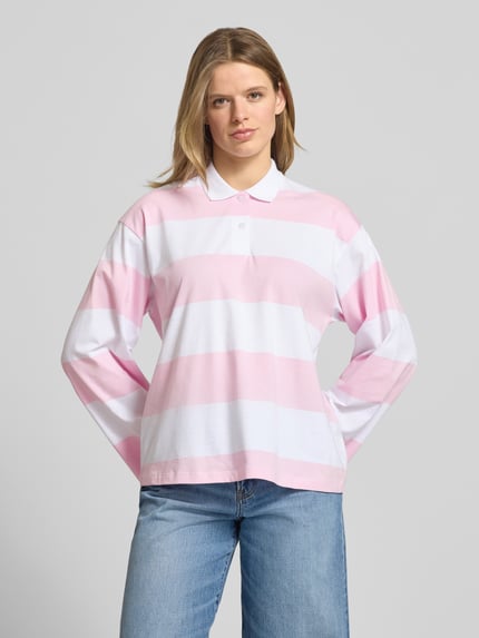 Vrouwenmodel draagt relaxed fit poloshirt uit puur katoen model 'VILMA' van JJXX, polokraag, met lange mouwen, ruglengte maat S 62 cm, brede roze-witte strepen, voorkant, borst-opname.
