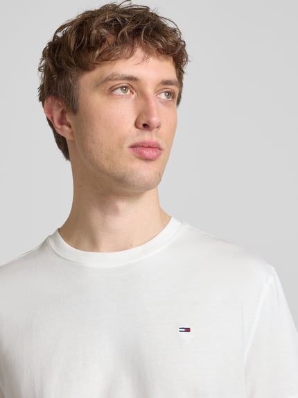Männermodel trägt Regular Fit T-Shirt aus reiner Baumwolle von Tommy Jeans, unifarben, Logo-Stitching, Nahaufnahme Oberkörper.