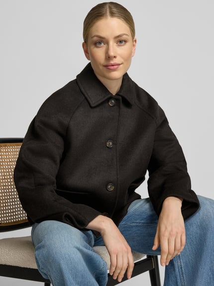 Frauenmodel trägt Relaxed Fit Jacke mit Woll-Anteil von Christian Berg Woman Selection in Schwarz, strukturierte Oberfläche, Nahaufnahme Oberkörper. Damen Jacke, Material-Mix mit Woll-Anteil, Umlegekragen, aufgesetzte Taschen, durchgängige Knopfleiste, Maße bei Größe 36: Rückenlänge 60 cm, Schulterbreite 45 cm, Brustweite 57 cm, Ärmellänge 60 cm.
