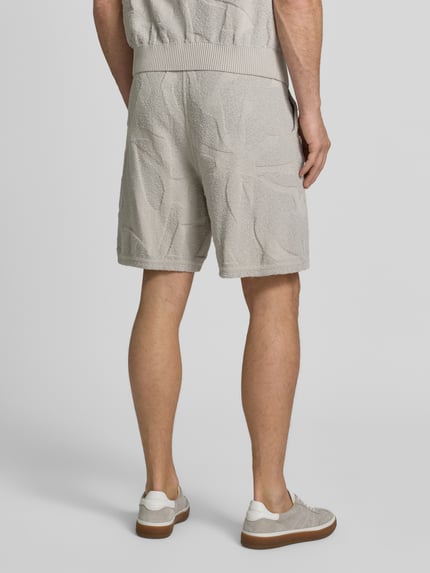 Männermodel trägt Regular Fit Sweatshorts aus Baumwoll-Mix Modell 'ASURFER' von BOSS Orange, Optik: Unifarben, Struktur, Label-Patch, Bundabschluss elastisch mit Tunnelzug, Eingrifftaschen, Materialverarbeitung: Frottee, Farbe beige, Ganzkörperansicht Rückansicht.