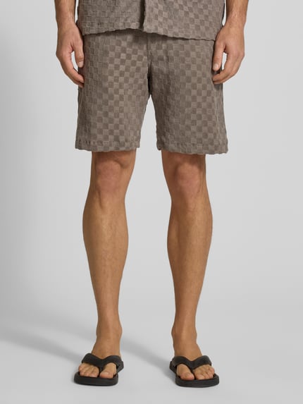 Männermodel trägt Regular Fit Shorts mit Label-Patch von Lindbergh in Braun mit Karomuster, Baumwoll-Mix, Nahaufnahme Oberschenkel, Vorderansicht.