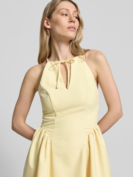 Frauenmodel trägt Cocktailkleid mit Schlüsselloch-Ausschnitt von Little Mistress in zartem Gelb, Material-Mix mit Rayon-Anteil, A-Linie, Minikleid, Schnürung und rückseitigem Reißverschluss, Rückenlänge 83 cm, Brustweite 40 cm, Nahaufnahme Oberkörper.