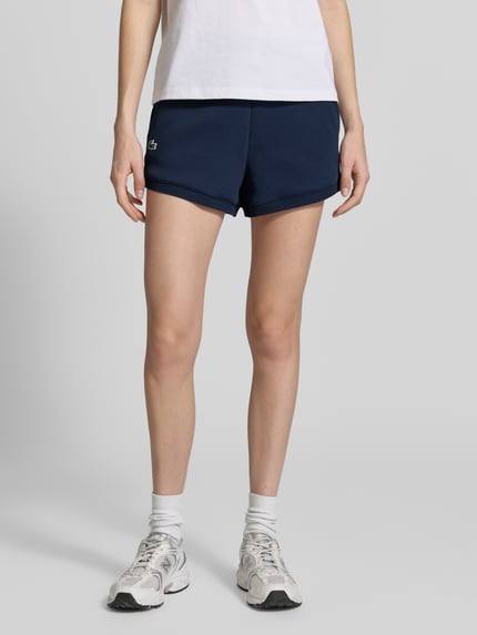 Frauenmodel trägt Regular Fit Sweatshorts mit Logo-Applikation von Lacoste, Optik: Unifarben, Sweat, seitliche Eingrifftaschen, Ganzkörperansicht von vorne.