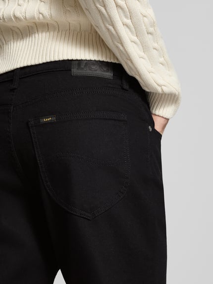 Männermodel trägt Tapered Fit Jeans mit Label-Patch Modell 'David' von LEE, schwarze Denim-Optik, 5-Pocket-Design, Detailaufnahme Rückansicht.